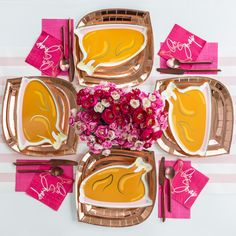 a table setting with pink and gold plates, napkins, and flowers on it