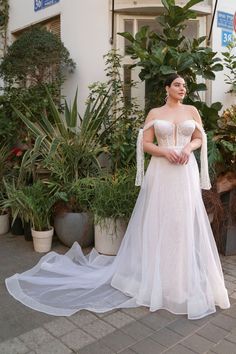 a woman in a wedding dress standing on the sidewalk next to some potted plants