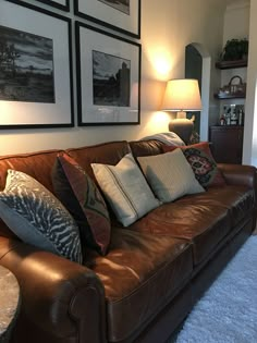 a brown leather couch sitting in a living room next to a lamp and pictures on the wall