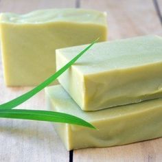 two bars of soap sitting on top of a wooden table next to a green leaf