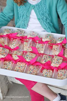 a woman holding a tray full of cake and sprinkles with pink ribbons