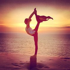 a woman doing a handstand on top of a wooden post in front of the ocean