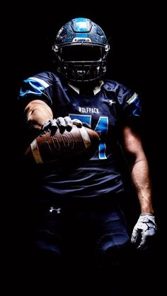 a football player holding a ball in his right hand and wearing a black uniform with blue lettering on it