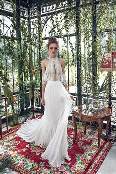 a woman in a white dress standing on a red rug with greenery behind her