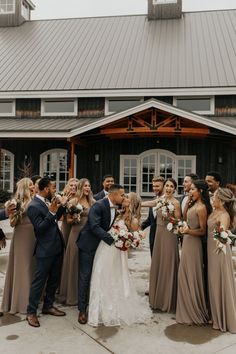 a group of people standing around each other in front of a building with a bride and groom