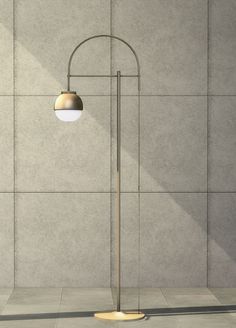 a floor lamp with a round light on it in front of a gray wall and tiled floor