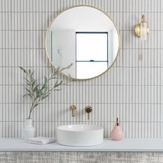 a white sink sitting under a round mirror next to a wall mounted faucet