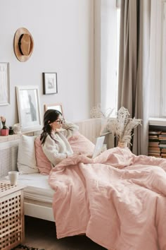 a woman sitting on a bed with a laptop in her hand and looking at the screen