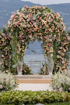 A romantic floral wedding arch adorned with roses and hydrangeas, set against a beautiful waterfront backdrop, creating a picturesque setting for an outdoor wedding ceremony. Upscale Wedding Decor, Floral Wedding Arch, Upscale Wedding, Wedding Arches Outdoors, Romantic Wedding Ceremony, 2024 Inspiration, Lights Wedding Decor