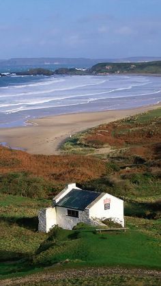 a small white house sitting on top of a lush green hillside next to the ocean