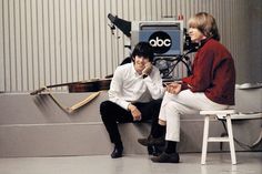 two people sitting on a bench in front of a recording equipment