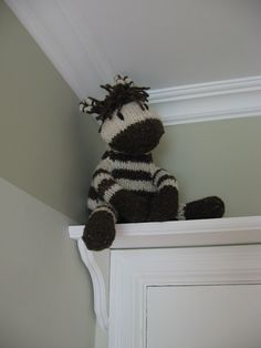 a stuffed zebra sitting on top of a white door frame in the corner of a room