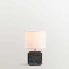 a black table lamp with a white shade on it's base and a wooden block underneath