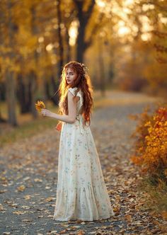 a woman with long red hair wearing a white dress and holding flowers in her hand