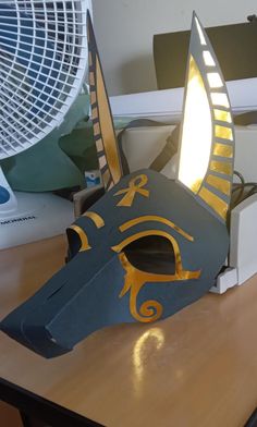 an egyptian mask sitting on top of a wooden table next to a fan and computer