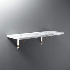 a white marble shelf with gold brackets on the wall in a gray room, next to a grey wall