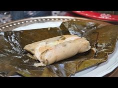 a piece of food sitting on top of a leafy green wrapper next to a red and white plate