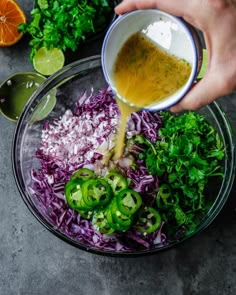 someone pouring dressing into a bowl filled with red cabbage, green onions and oranges