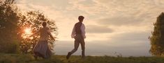 a man and woman are walking in the grass with trees behind them at sunset or dawn