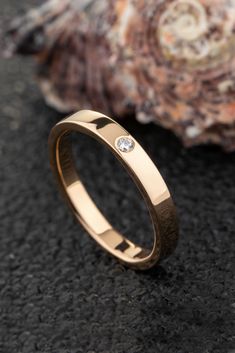 a gold wedding ring with a diamond on the side and a seashell in the background