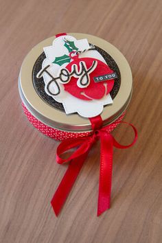 a small metal tin with a red ribbon around it that says joy on the lid