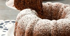 a chocolate bundt cake with powdered sugar on top and one slice being taken out