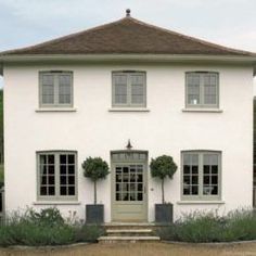 a large white house with three windows and two bushes in front of the entrance to it