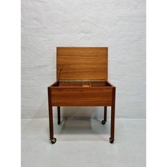 a small wooden table with wheels on the bottom and one drawer open to show something inside