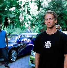 a man is standing in front of some parked cars and people are walking by him