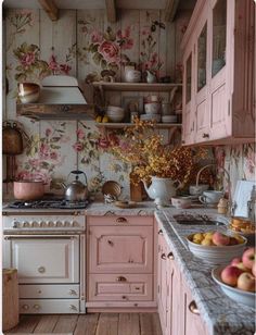 a kitchen with pink cabinets and flowers on the wall behind the stove top is filled with fruit