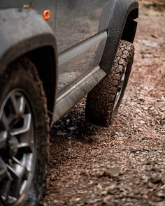 there is a black truck parked on the dirt road with it's tire missing