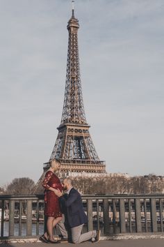 a man kneeling down next to a woman in front of the eiffel tower