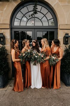 a group of women standing next to each other in front of a door holding bouquets