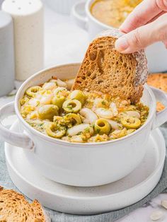 a person is dipping some bread into a bowl of soup with olives and cheese