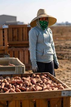 a woman wearing a face mask standing in front of a box full of potatoes on the beach