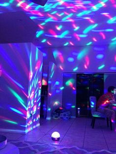 a man sitting in front of a laptop computer on top of a table under colorful lights