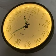 a clock with numbers on the face and hands is lit up in yellow light from below