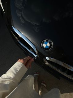 the front end of a black bmw car with someone's feet on the hood