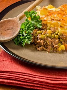 a plate topped with meat and vegetables next to a wooden spoon on top of a table