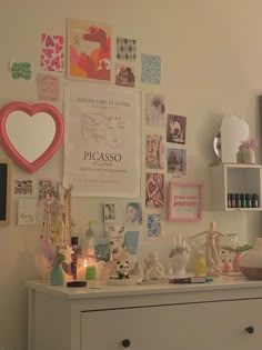 a white dresser topped with lots of clutter next to a wall covered in pictures