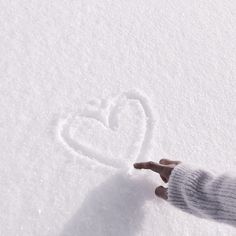 a person's hand is touching the snow with a heart drawn on it