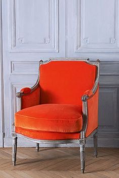 an orange chair sitting on top of a hard wood floor next to a white wall