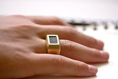 a person's hand wearing a gold ring with a black stone in the middle