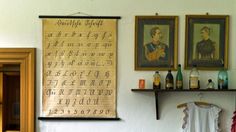 two framed pictures hang on the wall next to an old fashioned letter and number chart