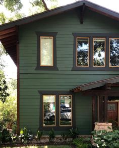 a green house with three windows and a car parked in the driveway