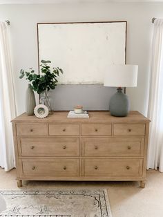 a wooden dresser with two vases and a plant on it in front of a large mirror