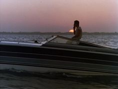 a man riding on the back of a boat while talking on a cell phone at sunset