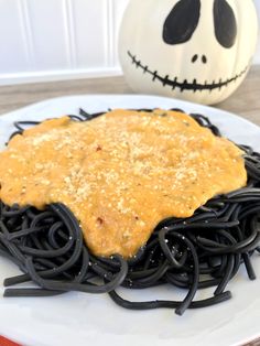 a white plate topped with pasta covered in cheese and black noodles next to a jack - o'- lantern