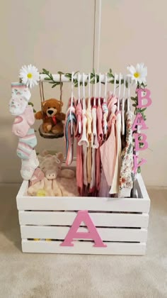 a baby's clothes rack with pink letters and flowers on the hangers, along with a teddy bear