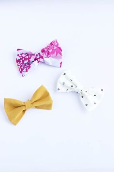 three bow ties sitting next to each other on top of a white surface with one yellow and the other pink